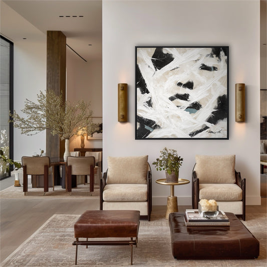 Large abstract painting on a white wall in a modern living room with beige armchairs and brown leather ottomans.