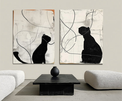 Original black cat diptych creates a bold, minimalist focal point over a dark rectangular table in a sleek, white lounge area.