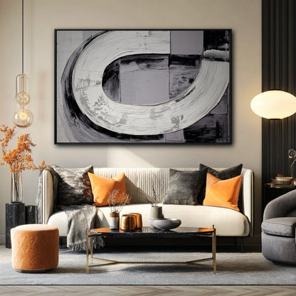 Large black and white abstract painting hanging above a sofa with bright orange pillows in a modern living room.