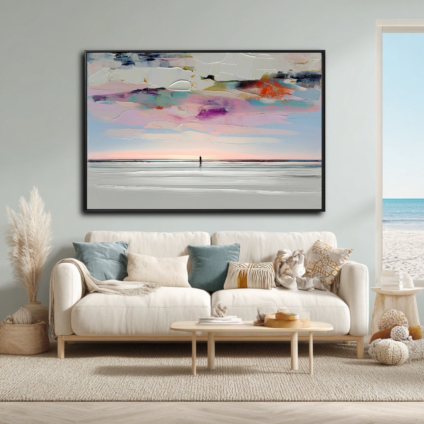 A large abstract beach painting hangs over a white sofa in a bright, coastal living room with an ocean view.