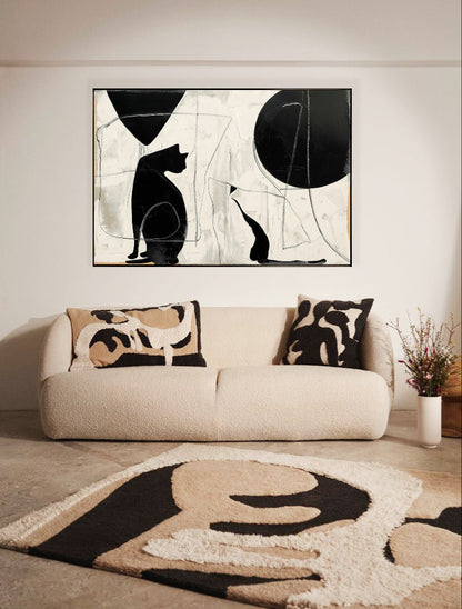 Modern black and white cat art hangs over a plush cream sofa, perfectly matching the abstract shapes on the cozy rug and pillows.
