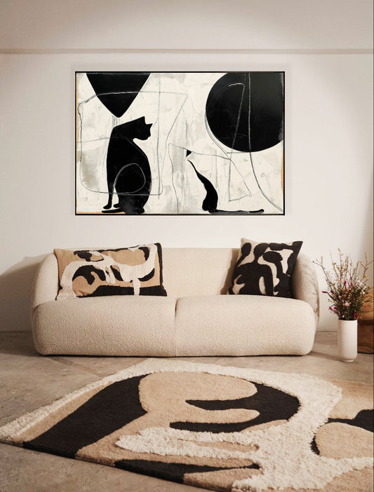 Modern black and white cat art hangs over a plush cream sofa, perfectly matching the abstract shapes on the cozy rug and pillows.