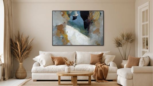 Abstract coastal art with yellow accents beautifully coordinating with the beige armchair and warm wood tones in a transitional setting.