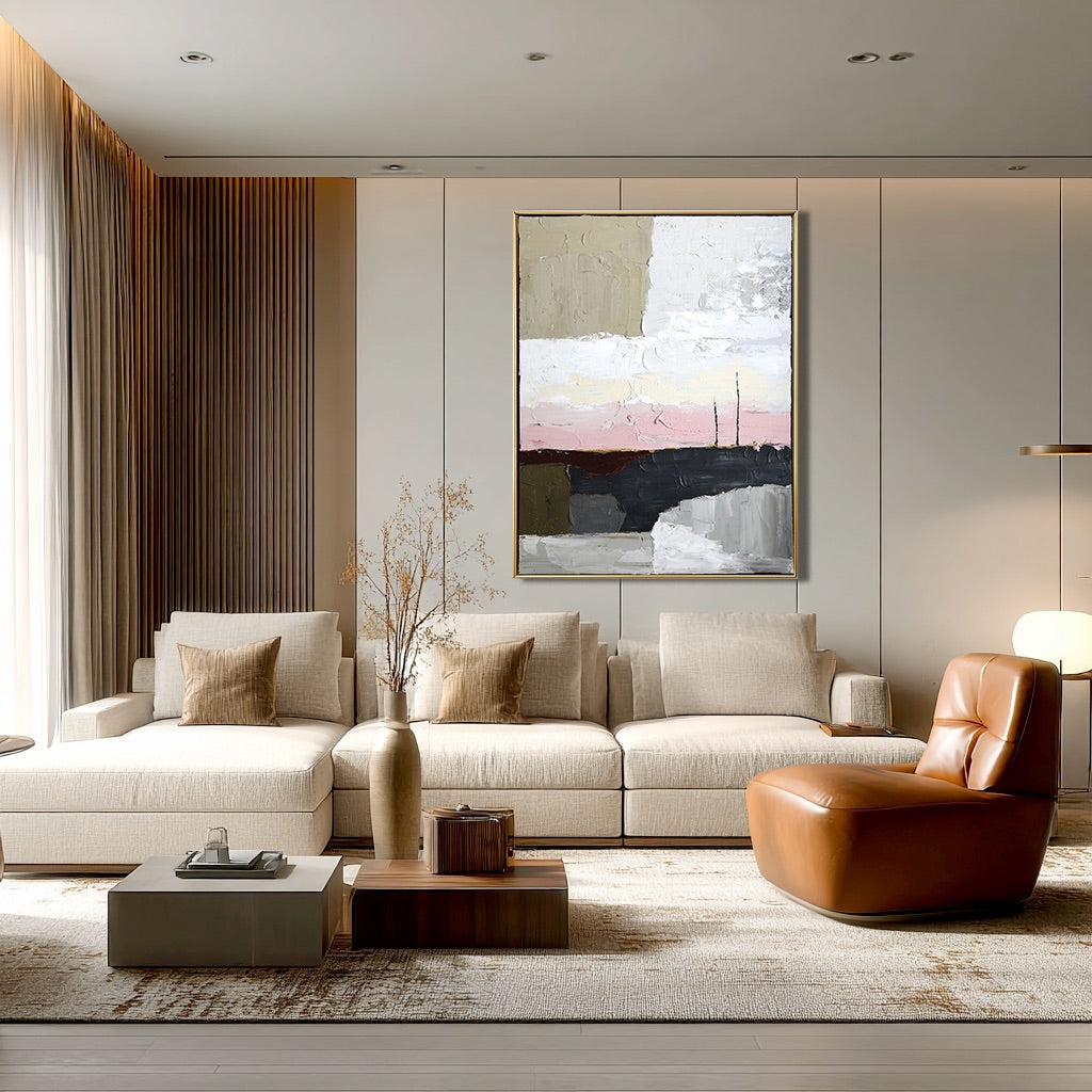 Original art over a light, modular sofa in a minimalist room with neutral tones, leather chair, and wood paneling.