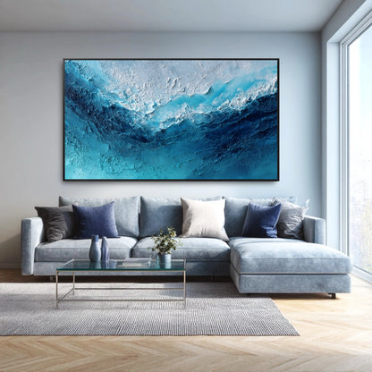 The large abstract ocean painting's blue and white tones perfectly complement the modern blue sectional and cool-toned living room.