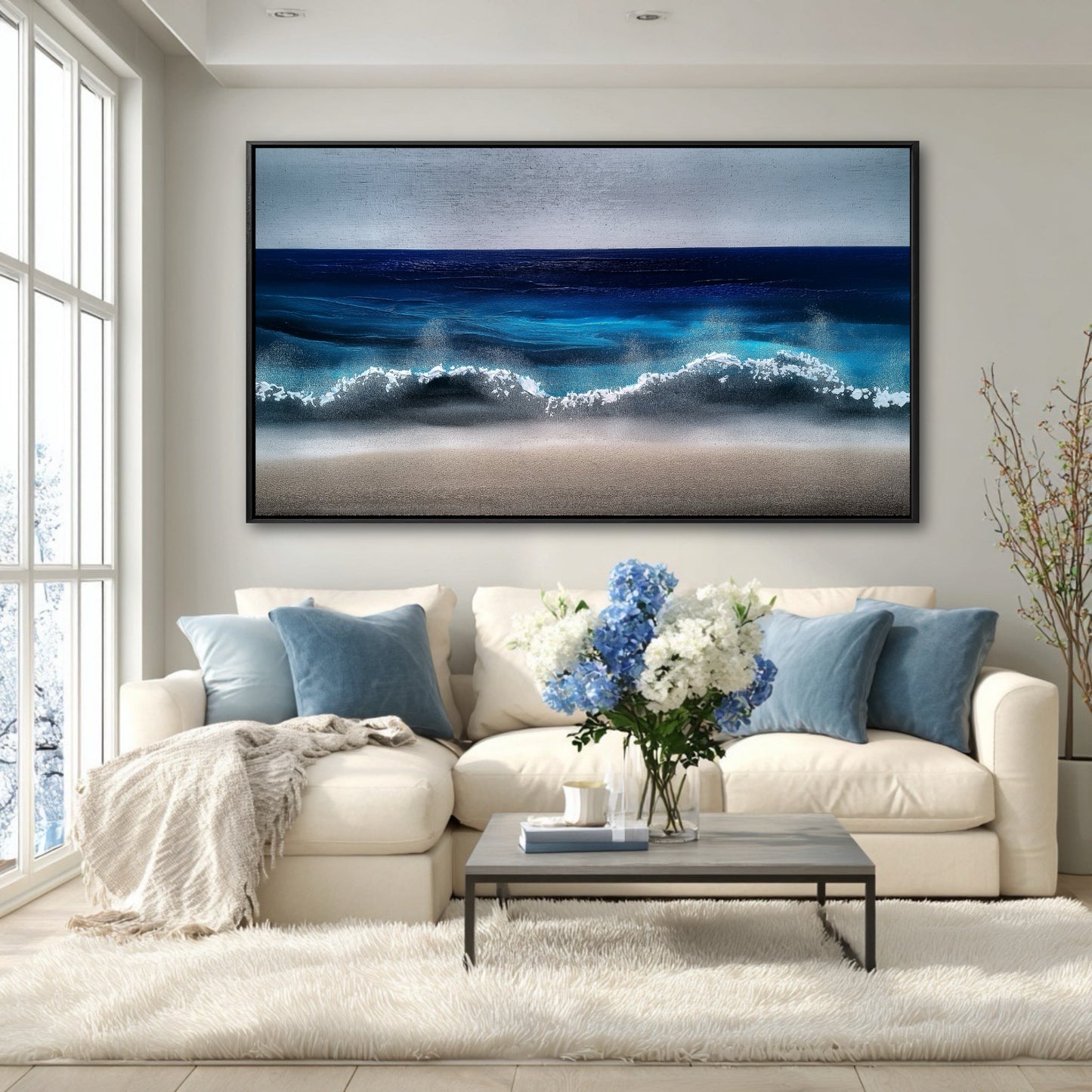 A large blue ocean painting hangs on a white wall above a white sectional sofa in a bright, airy living room.