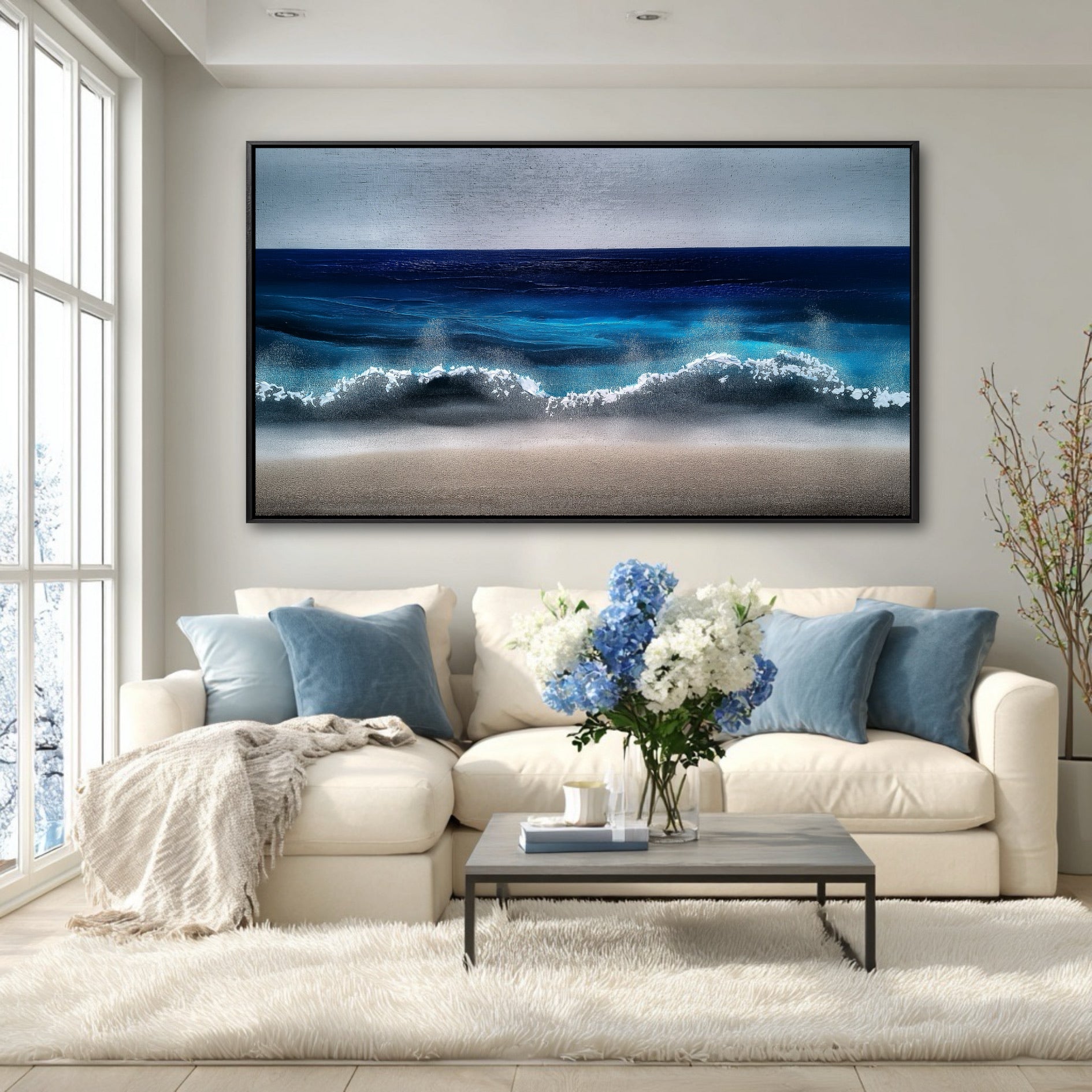 A large blue ocean painting hangs on a white wall above a white sectional sofa in a bright, airy living room.