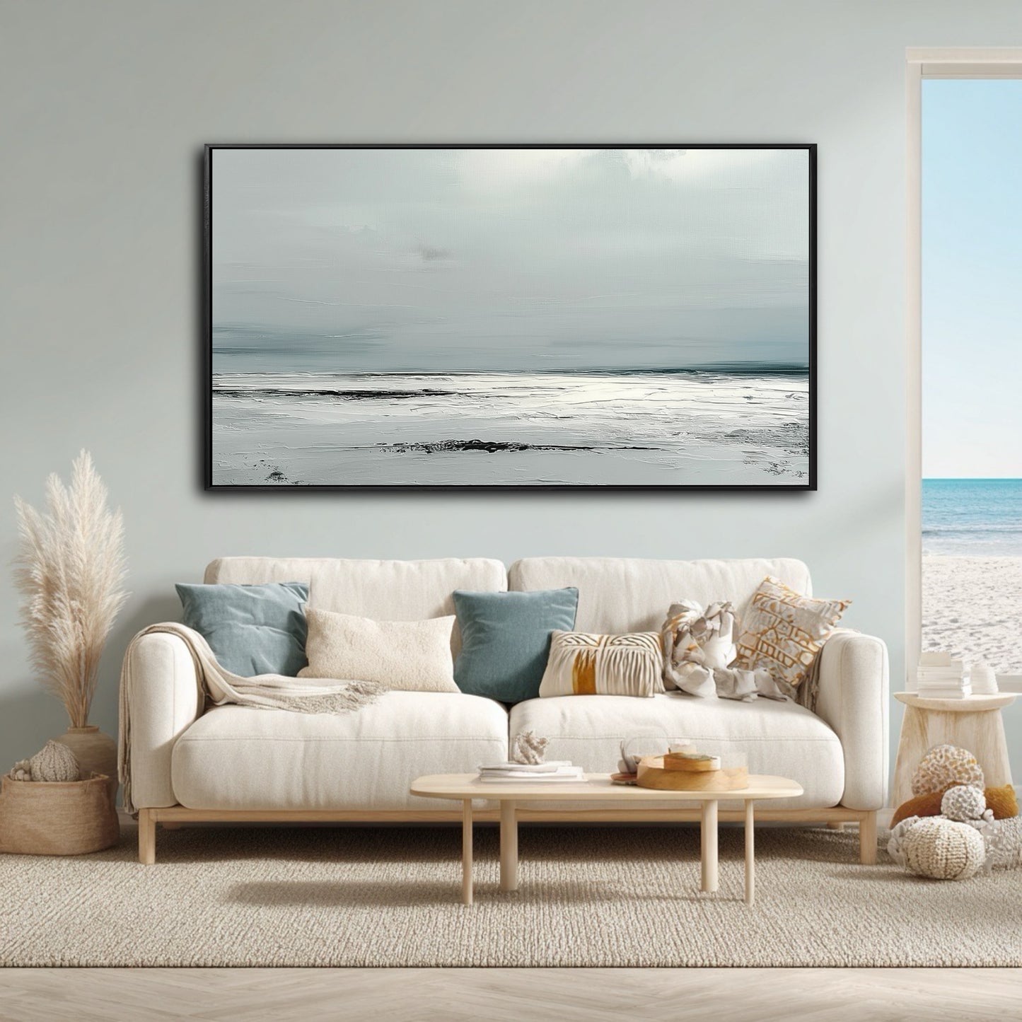 A large, minimalist gray seascape painting hangs above a white sofa in a bright, coastal living room with an ocean view.
