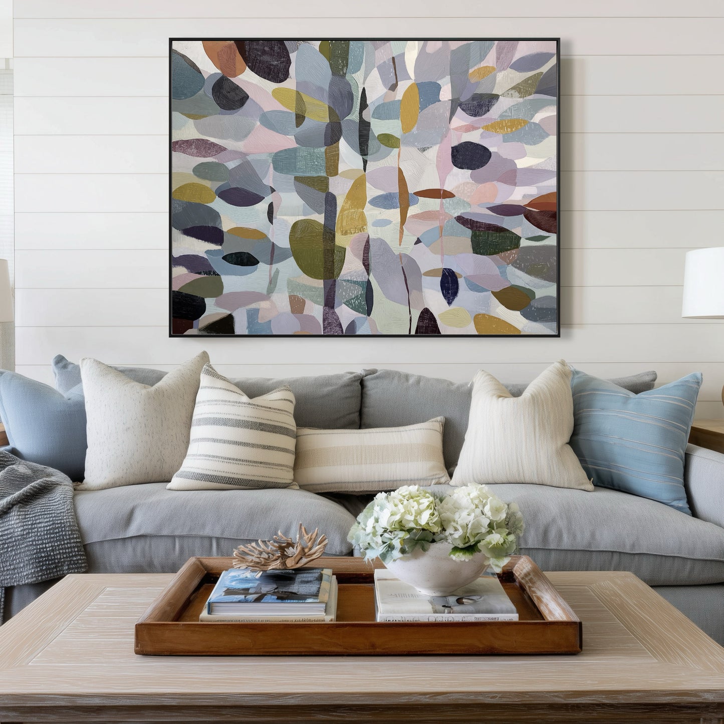 Original abstract art above a cozy gray linen sofa, adding a sophisticated color theme to the coastal farmhouse shiplap background.