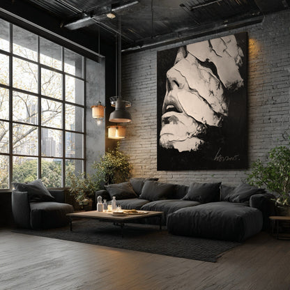 An oversized black and white abstract face painting hangs on a gray brick wall in a modern industrial loft with large windows.