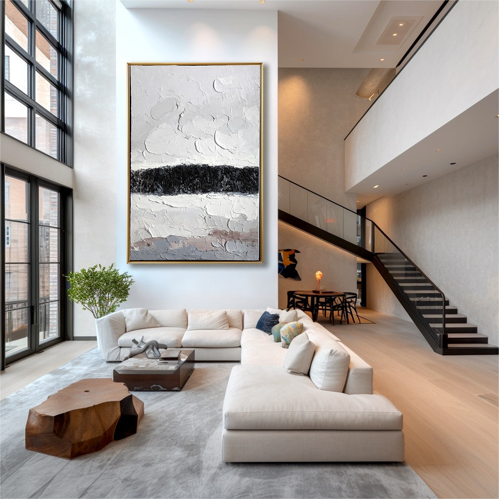 Original art in a dramatic double-height loft with huge windows, neutral sectional, and open staircase.