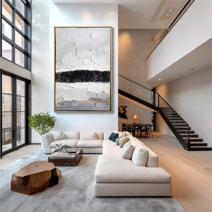 Original art in a dramatic double-height loft with huge windows, neutral sectional, and open staircase.