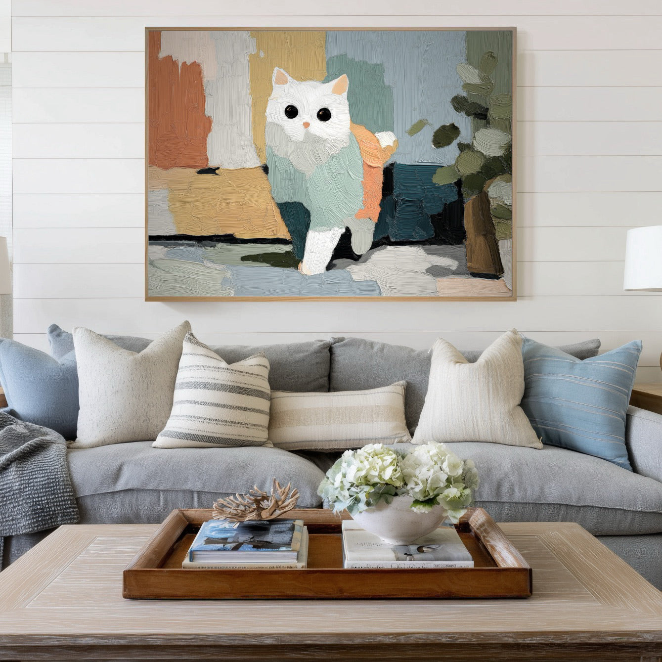 Horizontal abstract cat art centers a coastal cottage living room with shiplap walls, a gray linen sofa, and a light wood coffee table for a relaxed vibe.