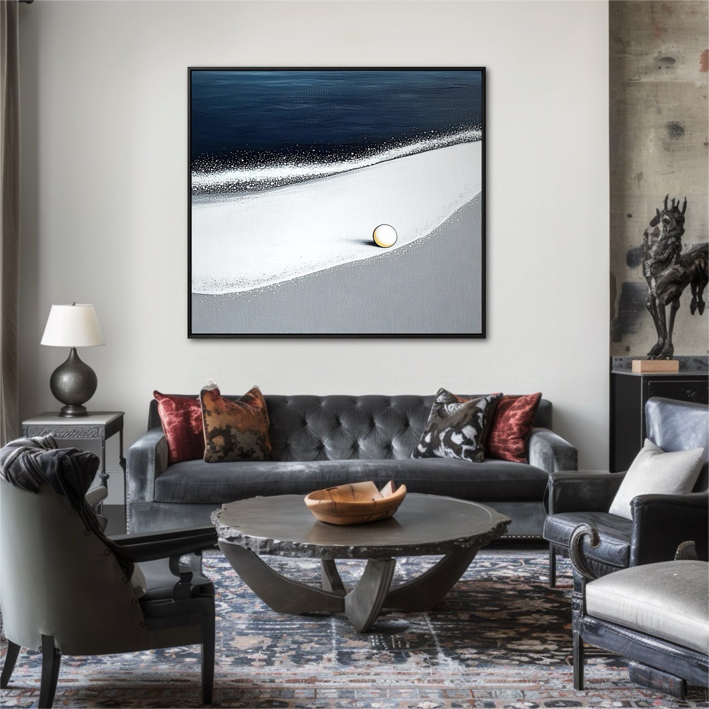 A modern abstract beach painting hangs above a grey velvet sofa in an eclectic, moody living room with a bronze statue.