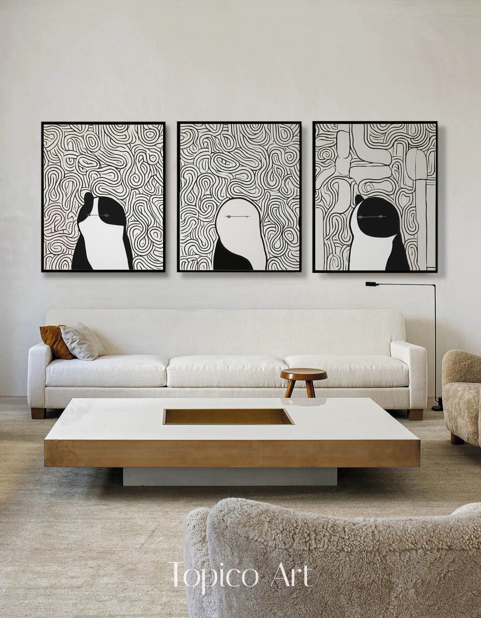 Monochromatic abstract cat triptych over a long white sofa, grounding a spacious living room with a clean, artistic focal point.