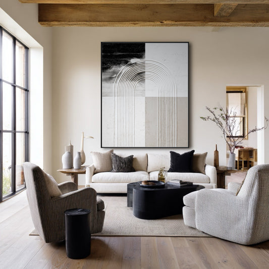Large abstract geometric art hangs in a rustic modern living room with exposed wood beams, a white sofa, and grey armchairs.