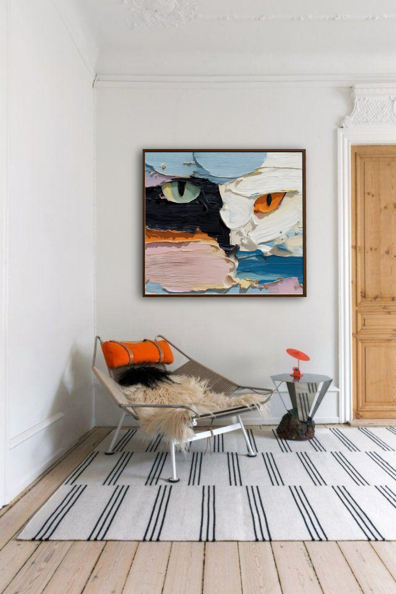 Textured cat portrait over a low sling chair, providing a vibrant pop of abstract art to a crisp, minimalist white room with a striped rug.