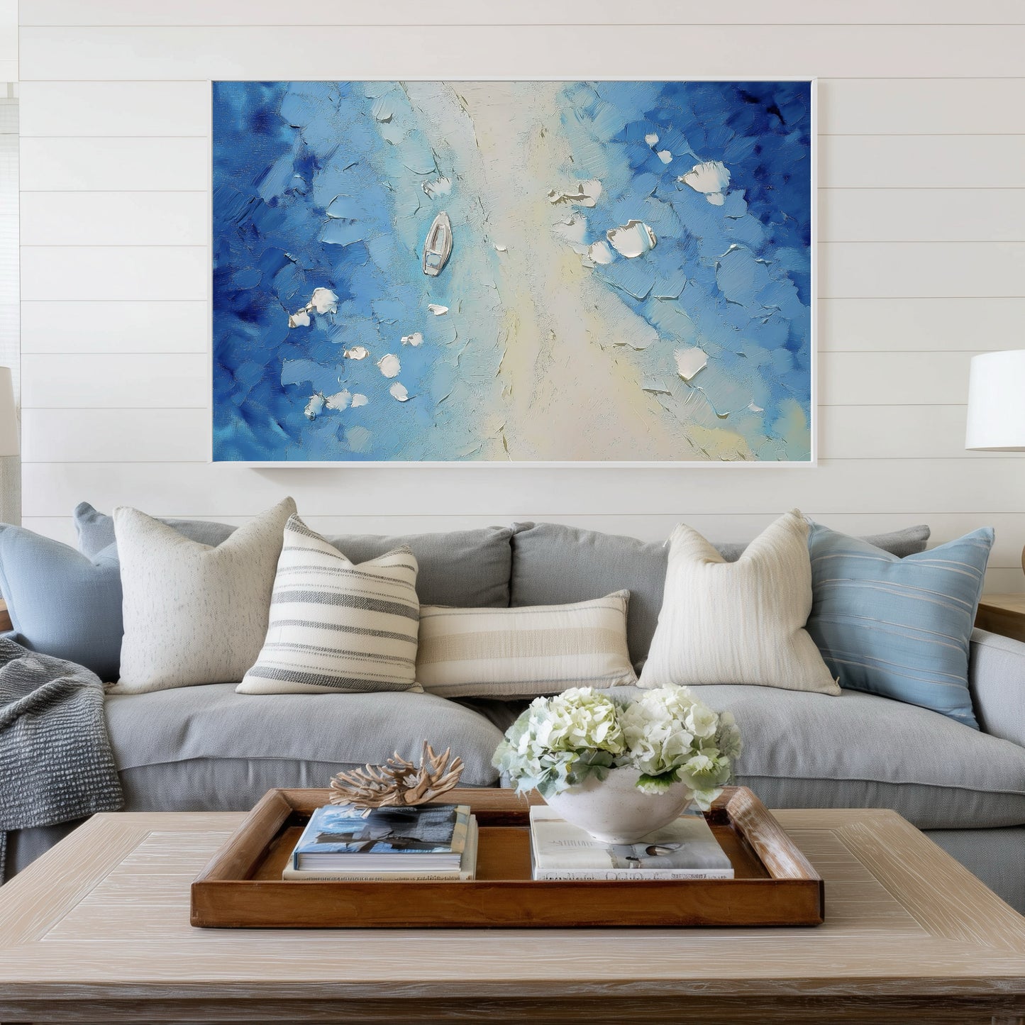 Textured blue seascape art completing the coastal aesthetic above a grey sofa, harmonizing with shiplap walls and striped nautical pillows.