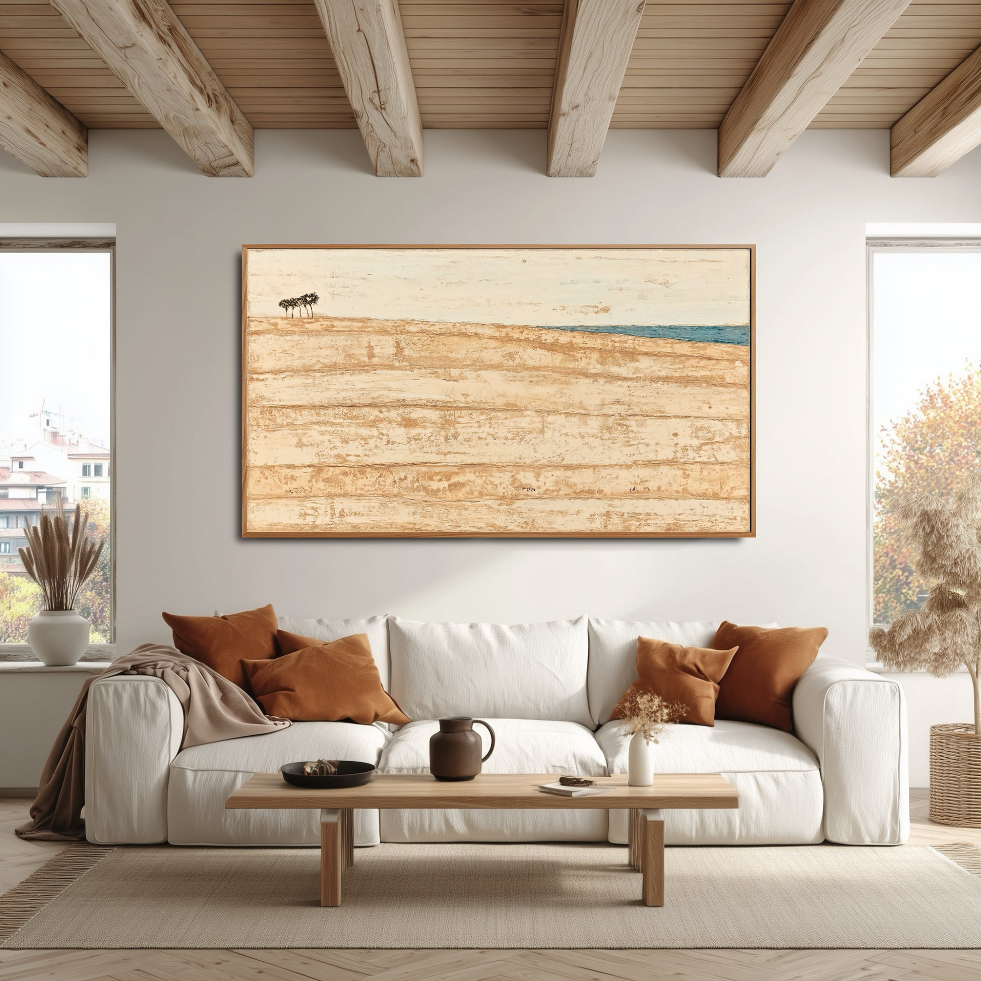 Gold-toned abstract art perfectly mirrors the warm wood ceiling beams and accent pillows over the white sofa in this bright space.