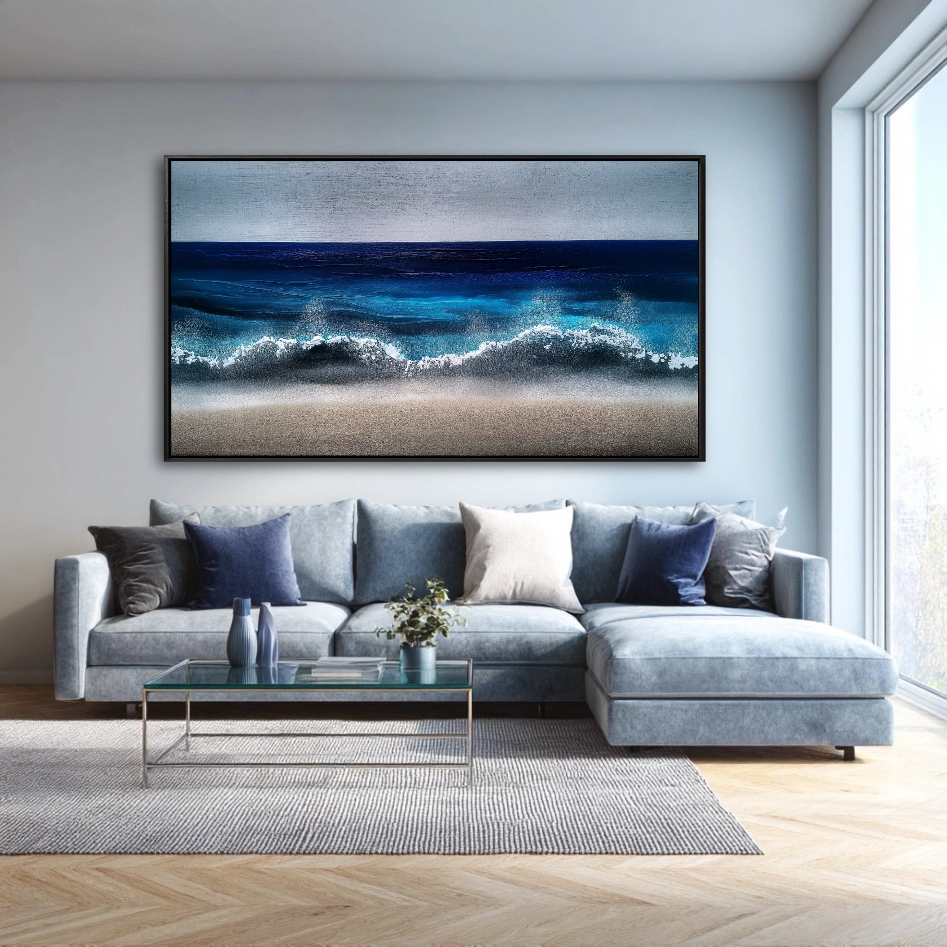A large, modern blue ocean painting hangs above a light blue-gray sectional sofa in a bright, contemporary living room.