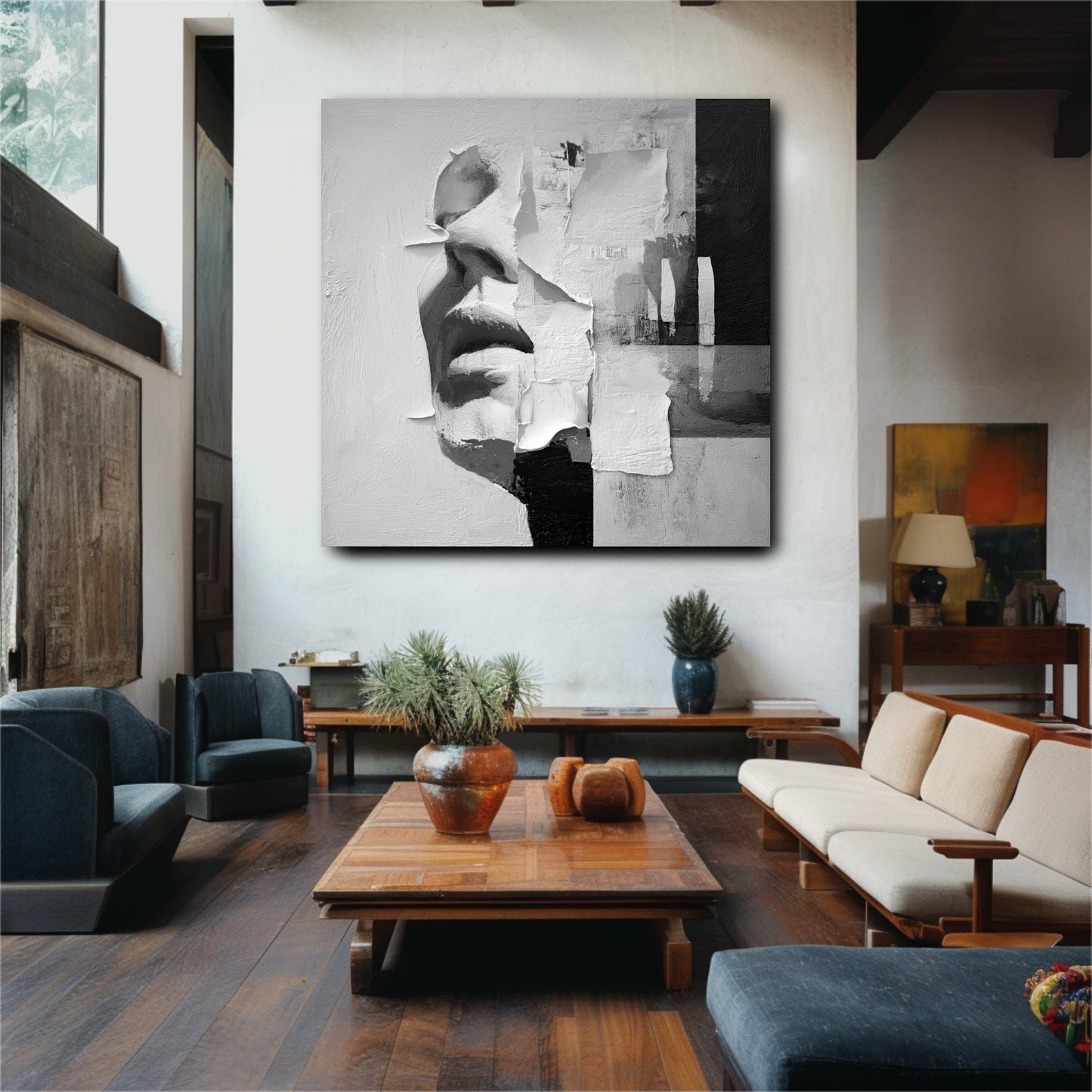 Large black and white abstract face painting hanging in a modern living room with dark wood floors and blue accent chairs.