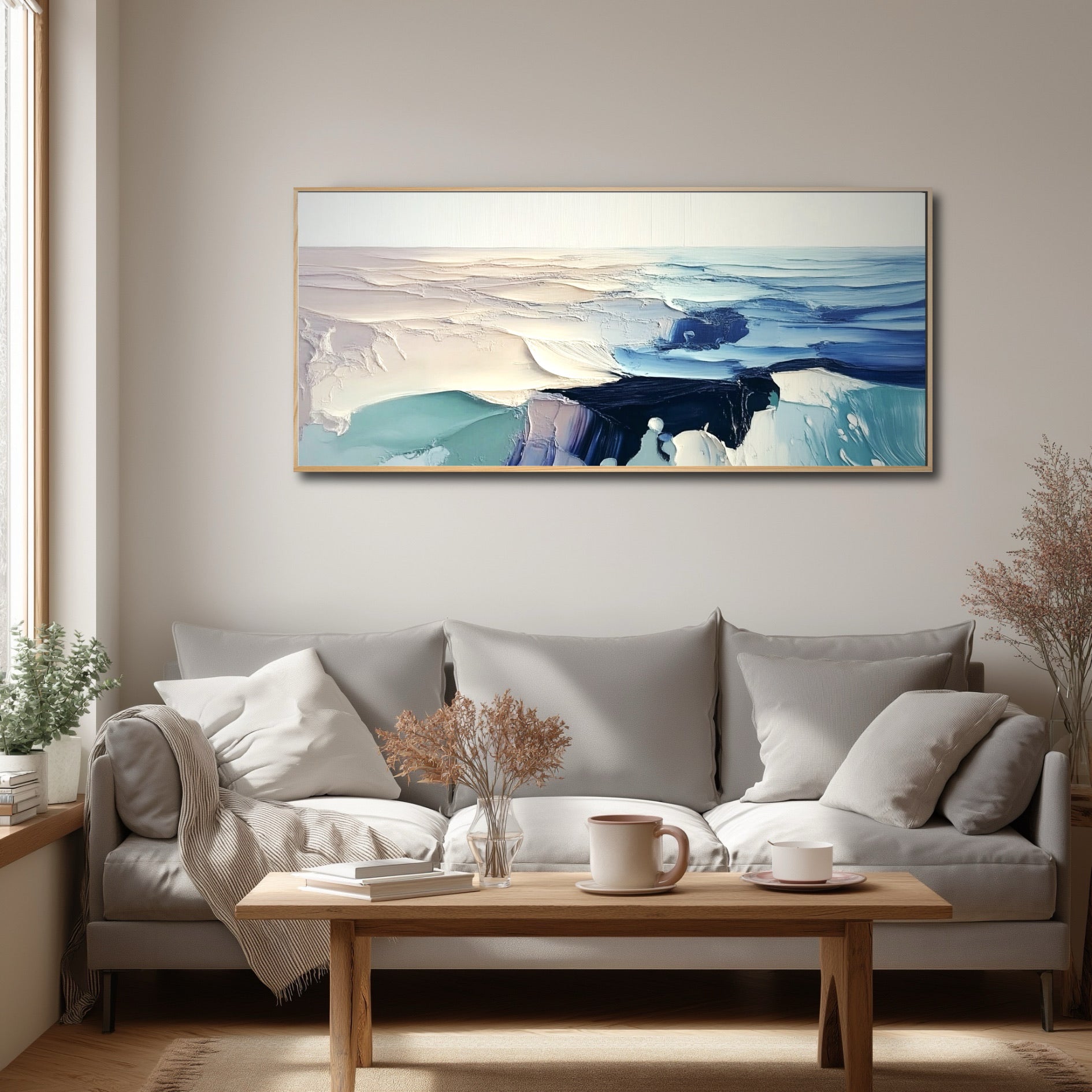 Bright, neutral living room with a grey sofa and wood coffee table, featuring a large abstract ocean painting by a window.