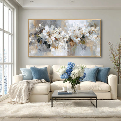 A large neutral abstract painting balances the cool blue accents of the pillows and flowers in a bright, modern living room with a large window.