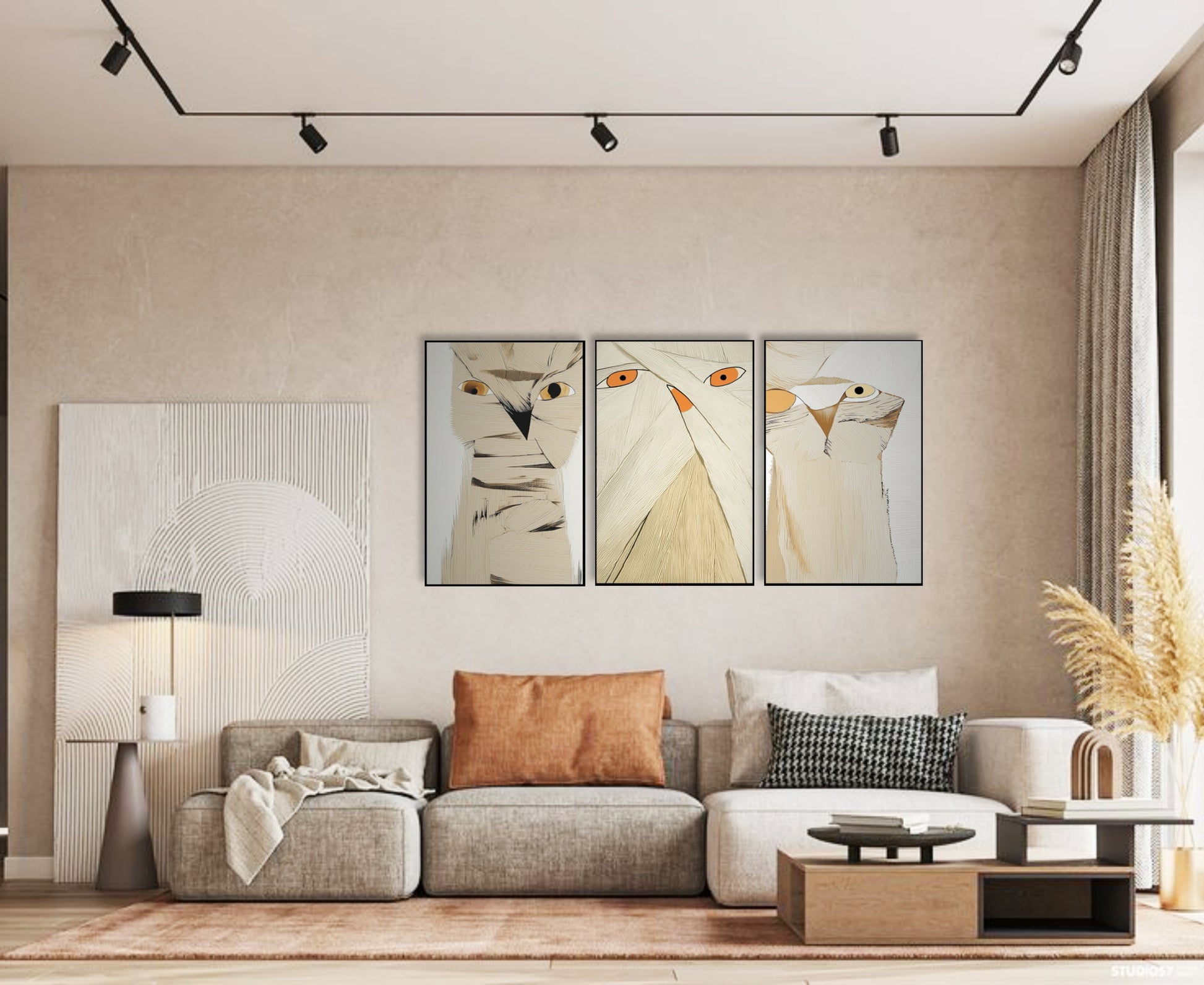 Neutral-toned owl art triptych above light grey sectional, accent pillows, track lighting, and beige wall in a minimalist living room.