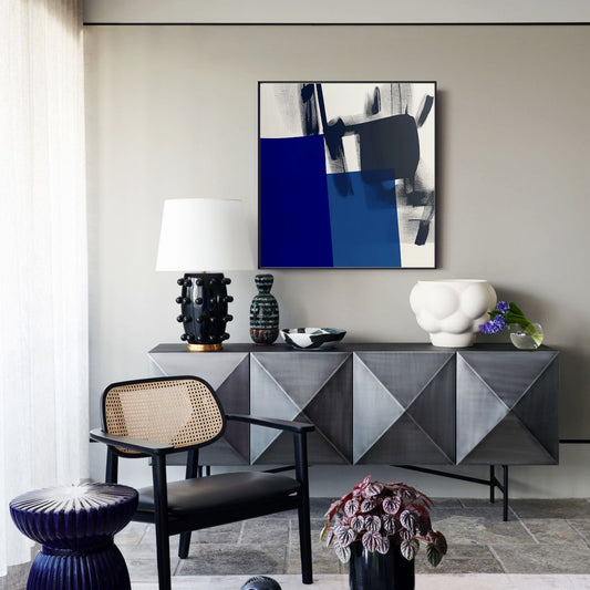 Bold blue abstract painting hangs above a striking geometric credenza, enhancing the modern, eclectic style of a sophisticated foyer space.