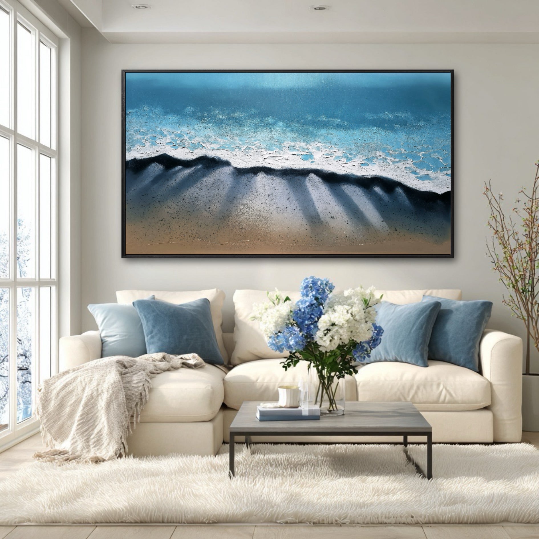 A large beach painting's deep blue and shadow details create a serene focal point in a bright, modern room with a white sectional.