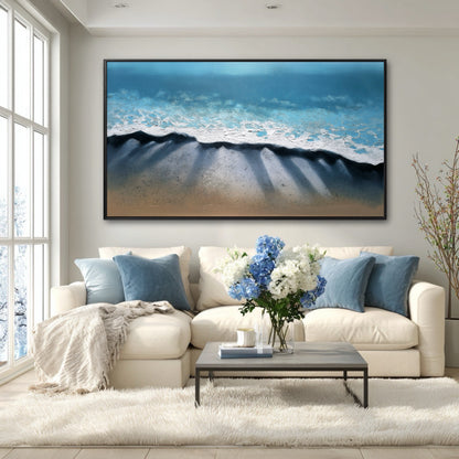 A large beach painting's deep blue and shadow details create a serene focal point in a bright, modern room with a white sectional.