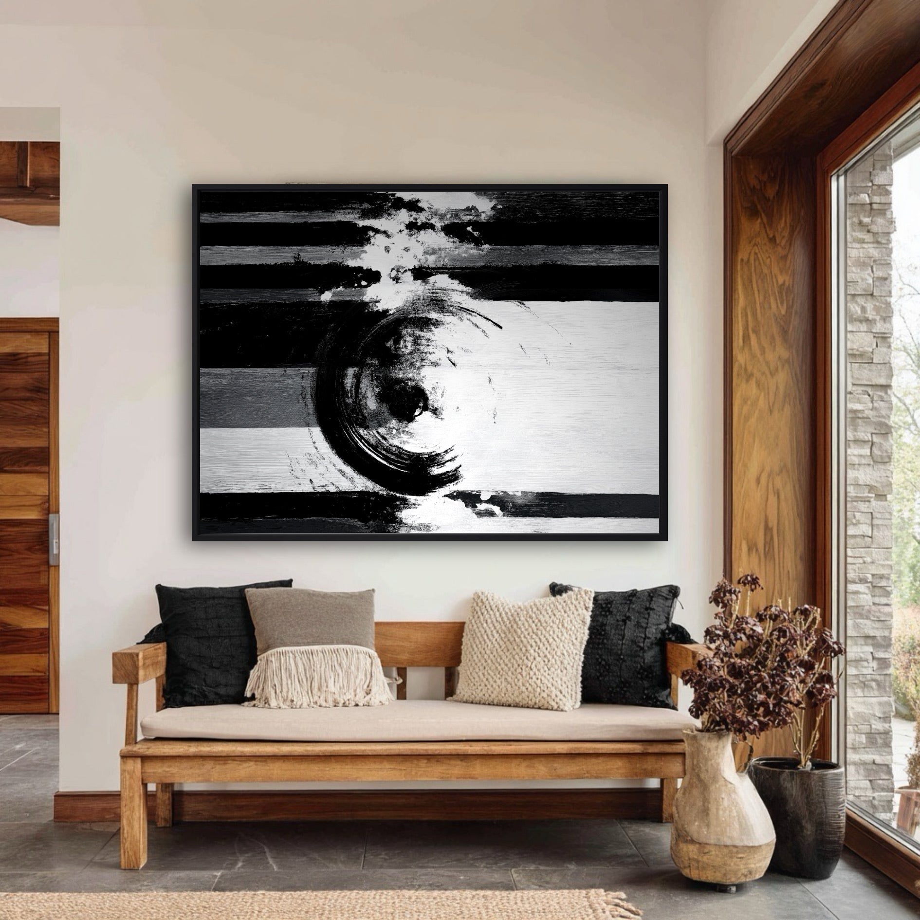 Large horizontal black and white painting above a natural wood bench with textured pillows in a rustic modern entryway.