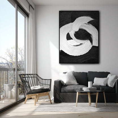 Vertical black and white abstract art on a white wall in a modern apartment with a grey sofa and a balcony.
