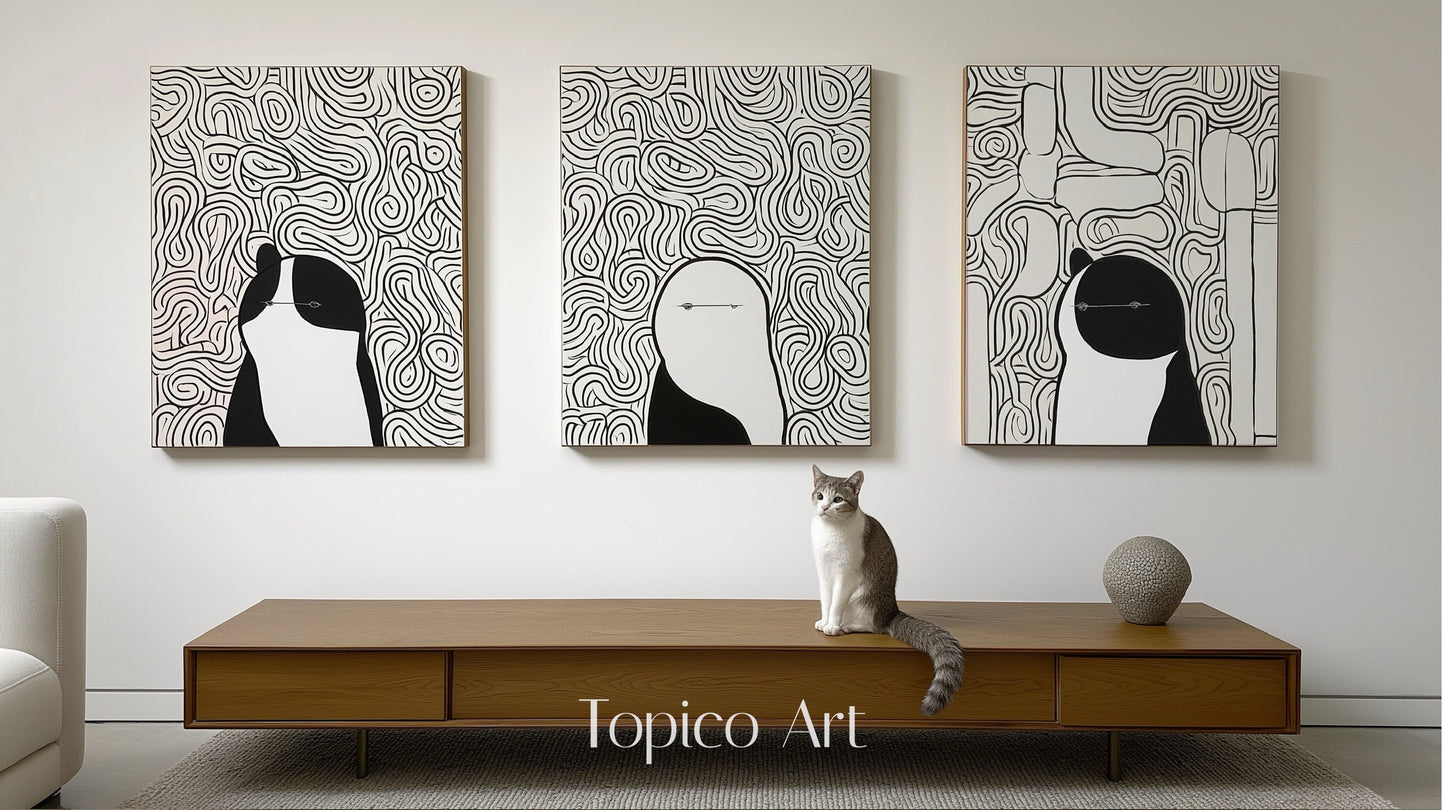 Three modern black and white canvases featuring abstract figures/animals, centered over a wood console table with a gray and white cat.